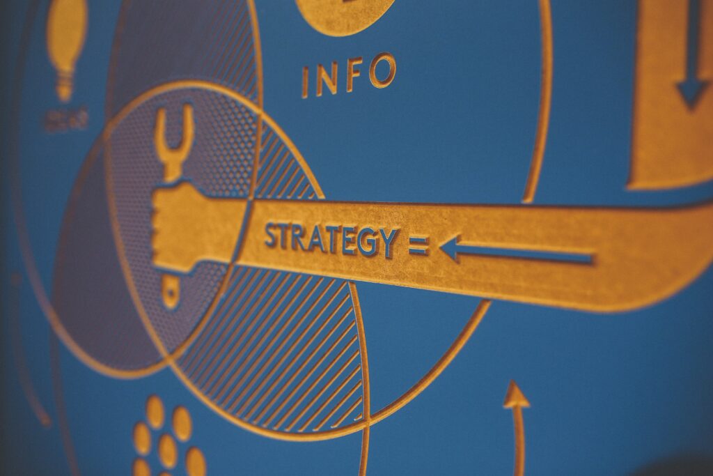 Close-up of a blue and orange graphic featuring overlapping circles, a hand holding a wrench, and the word STRATEGY = with an arrow pointing right. The word INFO appears above the circles.