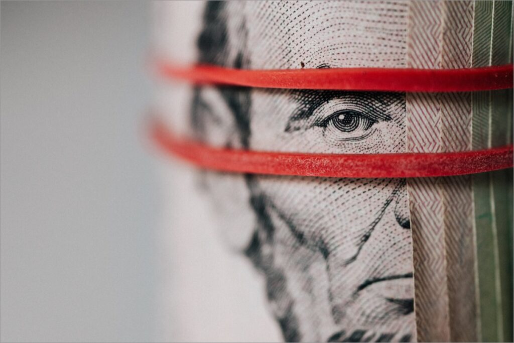 A close-up of a rolled stack of U.S. five-dollar bills secured with red rubber bands, showing part of Abraham Lincolns face.
