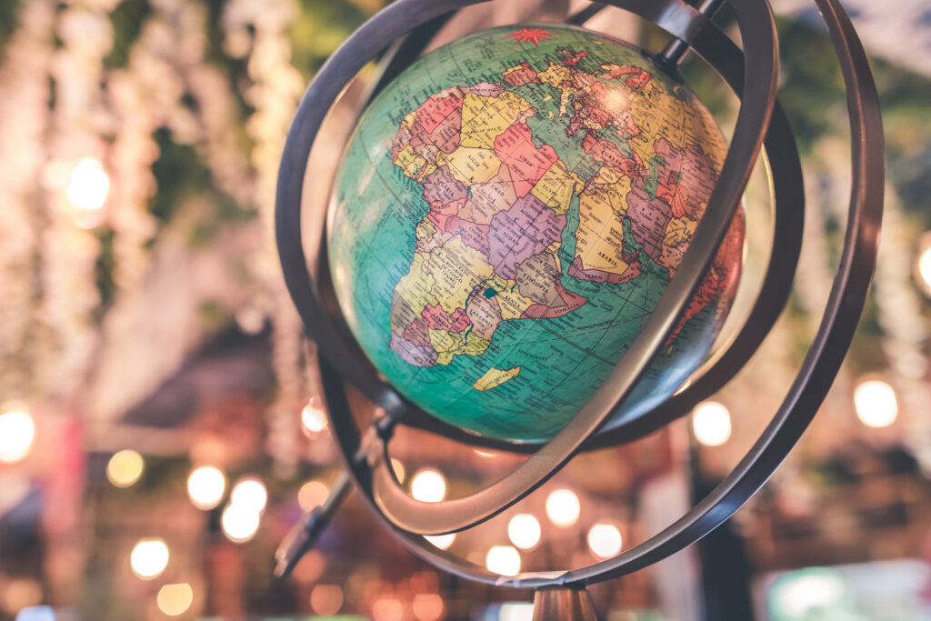 A colorful globe focused on Africa and Europe sits in a metal frame, with blurred warm lights and hanging greenery in the soft-focus background.