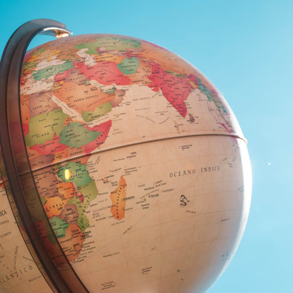 A close-up view of a globe showing parts of Africa, Europe, and Asia against a clear blue sky. The globe’s surface includes country names and boundaries, with the Indian Ocean labeled in the center.