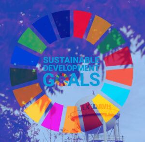 A colorful circular Sustainable Development Goals (SDG) logo overlays a photo of a UC Davis water tower with blue sky and tree branches in the background. The words “SUSTAINABLE DEVELOPMENT GOALS” appear in the center.