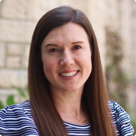 A woman with long brown hair and a striped shirt smiles at the camera. The background is softly blurred, showing a light-colored wall and some greenery.
